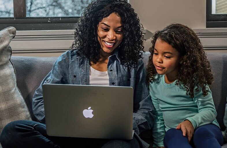 black female and daughter working on Apple computer in living room