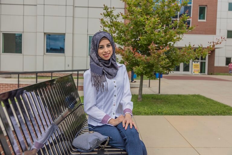 female student sitting outside on bench in front of campus building
