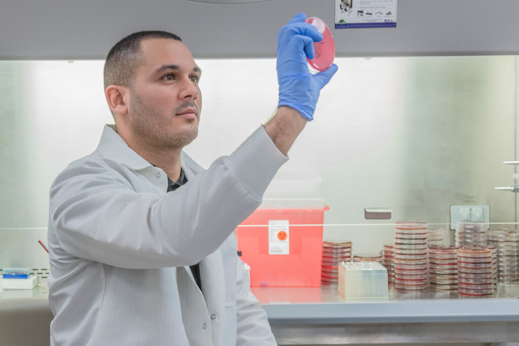 student in lab coat holding petri dish up to the light