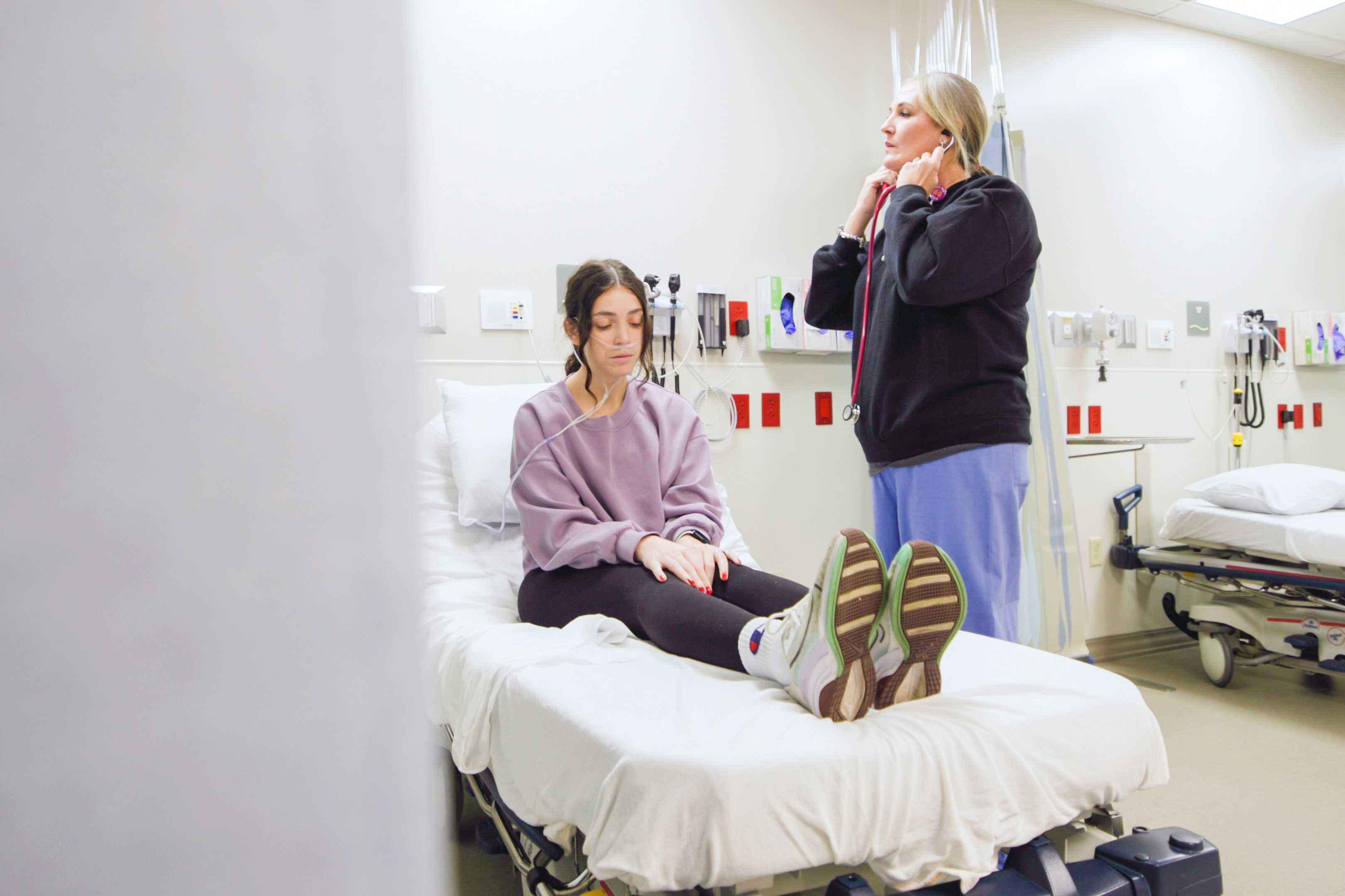 student practicing using a stethoscope on a patient sitting on a hospital bed